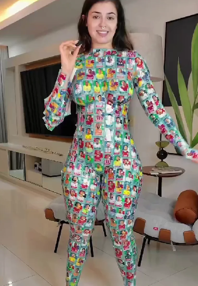 Una mujer sonriente posa de pie en un living luciendo un enterizo estampado con figuritas de futbolistas.