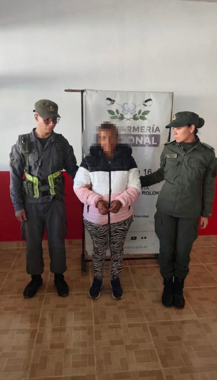 Dos gendarmes custodian a una persona con la cara pixelada frente a un cartel de Gendarmería Nacional.