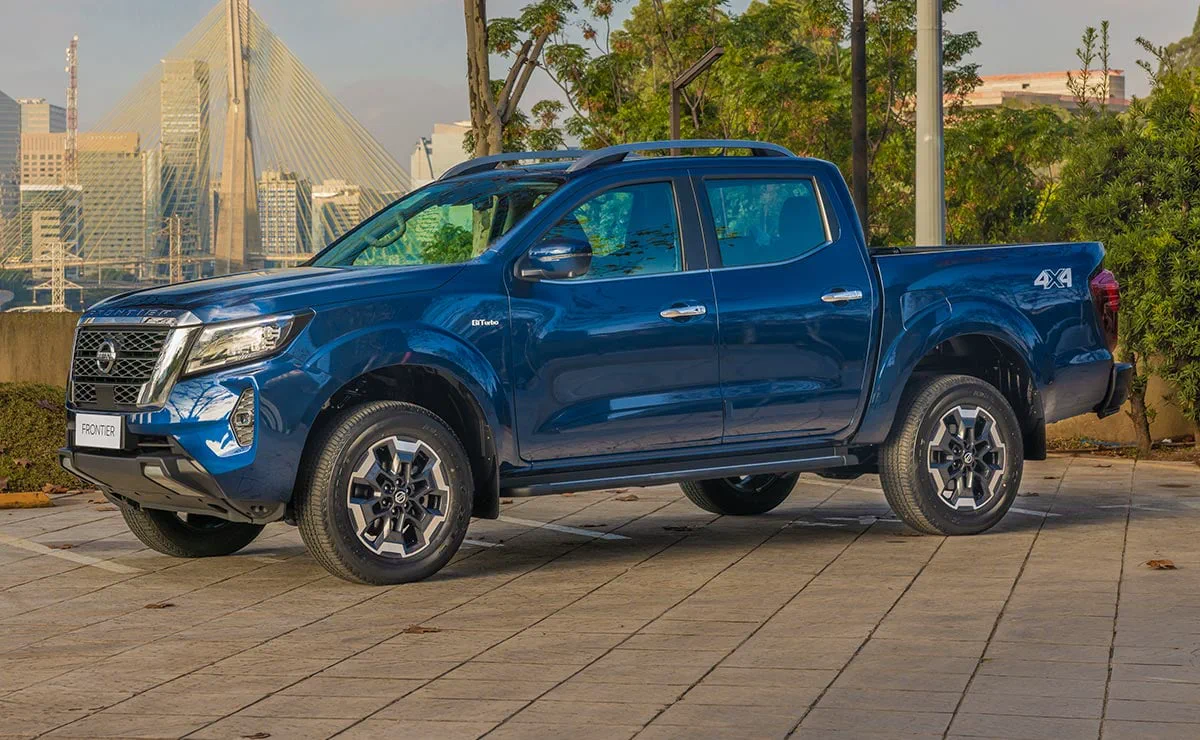Una camioneta azul de doble cabina permanece estacionada en una plazoleta frente a un puente atirantado.
