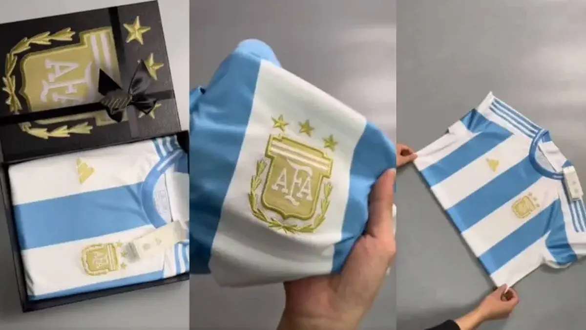Una camiseta de la selección argentina con tres estrellas y el escudo de la AFA en una caja de regalo y sostenida con las