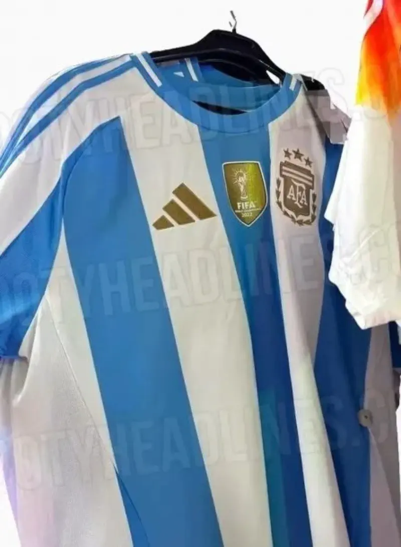 Una camiseta de fútbol de la selección argentina con tres estrellas y parche dorado cuelga de una percha.