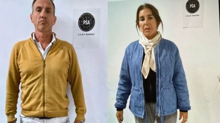 Un hombre con campera mostaza y una mujer con campera de jean posando frente a carteles de la Policía de Seguridad