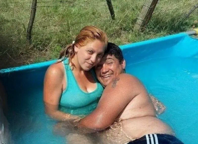 Un hombre y una mujer se abrazan sonrientes dentro de una pelopincho con agua en un patio.