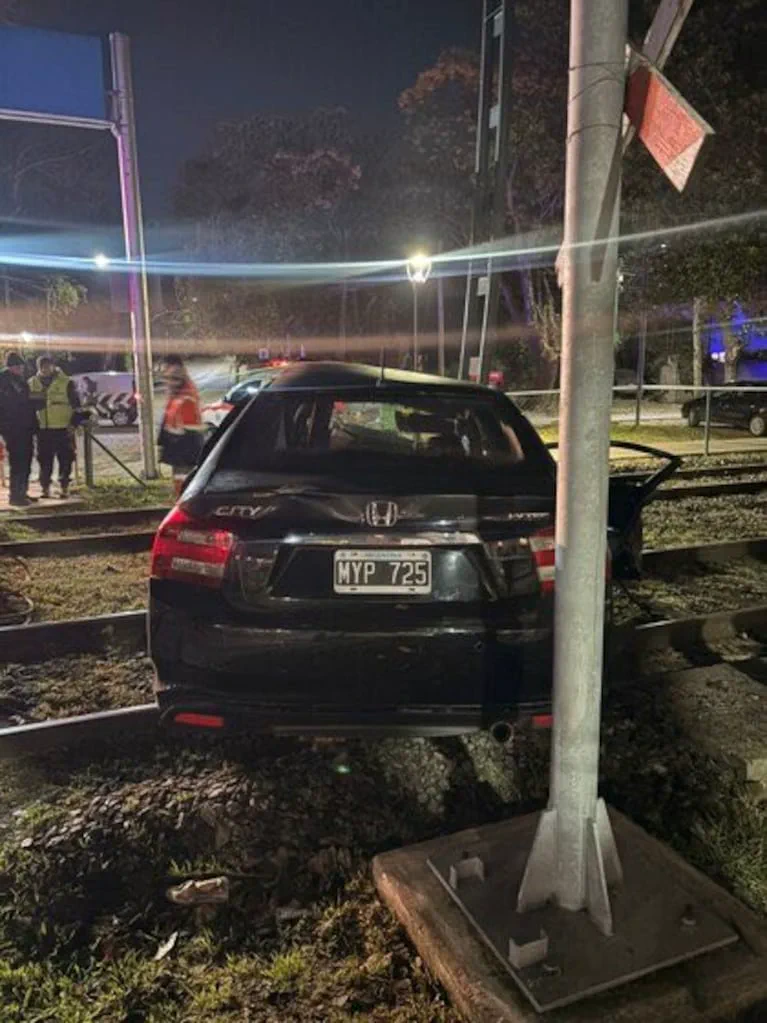 La parte trasera de un auto negro chocado sobre las vías del tren junto a un poste metálico.