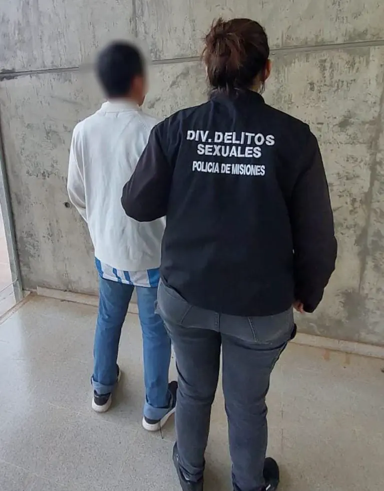 Una oficial de policia con campera de Delitos Sexuales traslada de espaldas a una persona demorada.