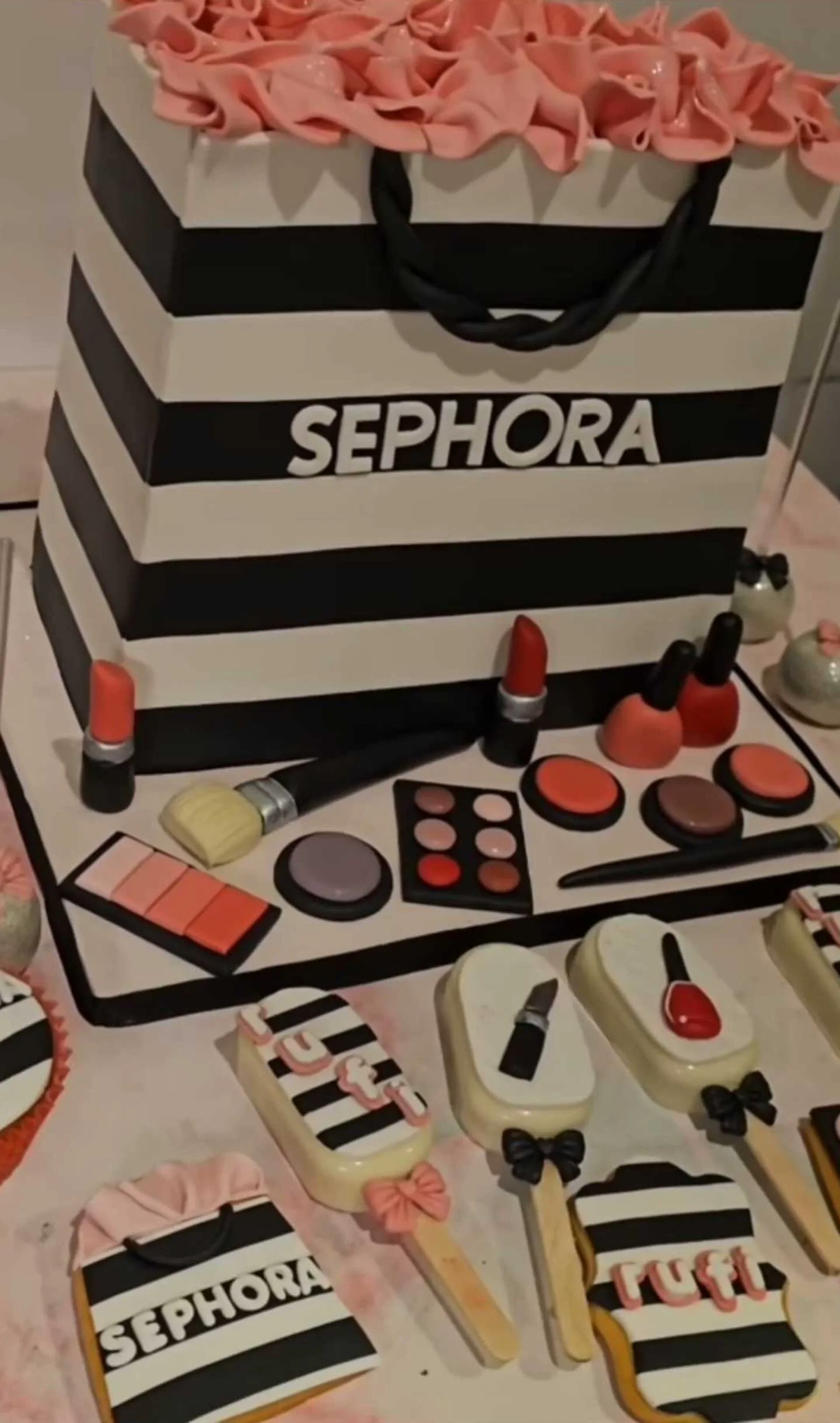 Torta con forma de bolsa de Sephora rodeada de galletitas y dulces con forma de maquillaje.