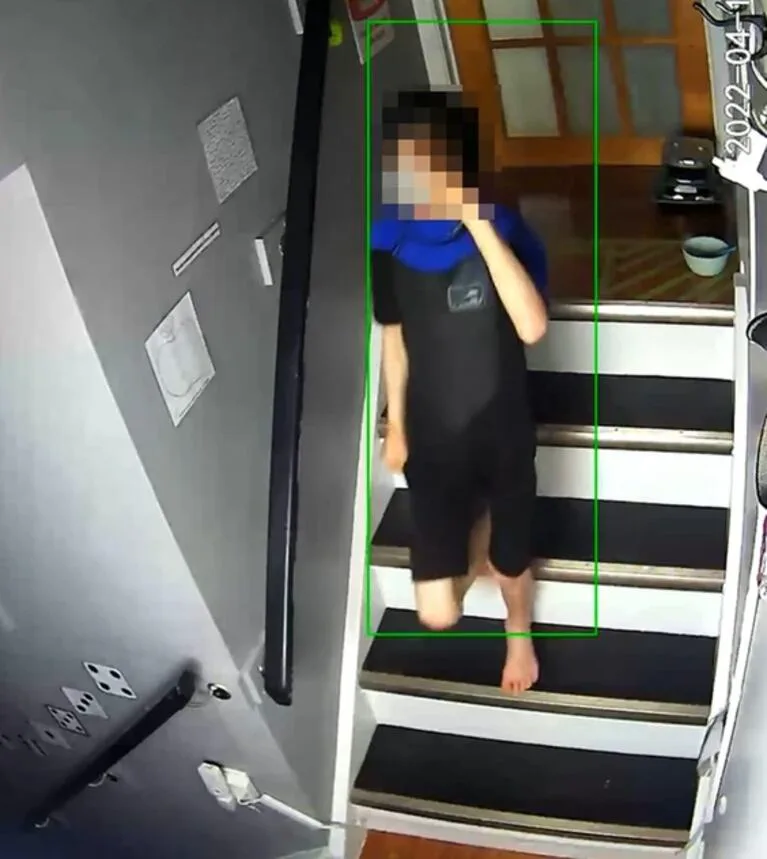 Una persona descalza baja por una escalera de madera con escalones negros dentro de una casa.
