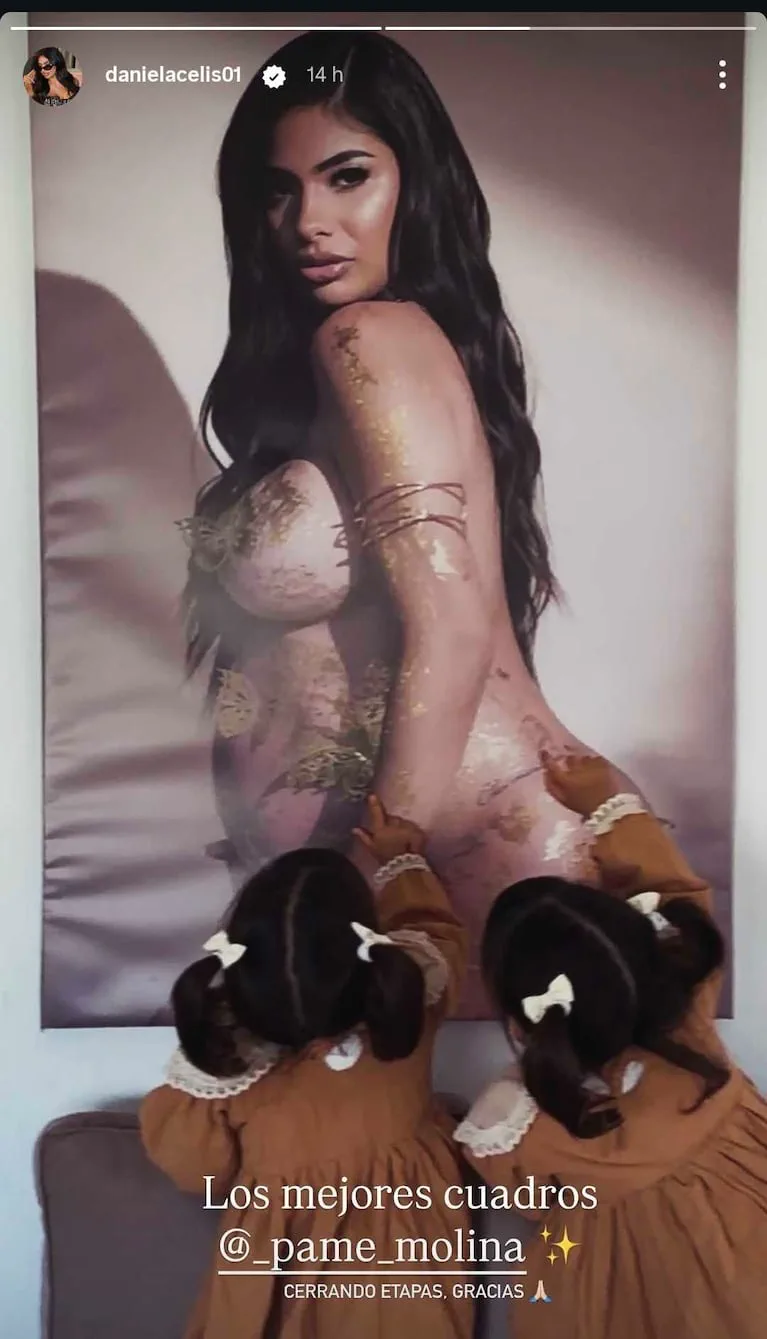 Dos bebas de espaldas tocando una foto grande de Daniela Celis embarazada colgada en la pared.