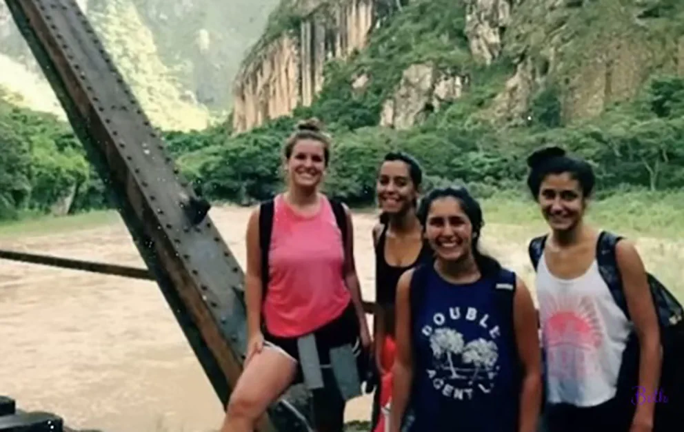 Cuatro mujeres jovenes posan y sonrien junto a una estructura metalica con un fondo montanoso.