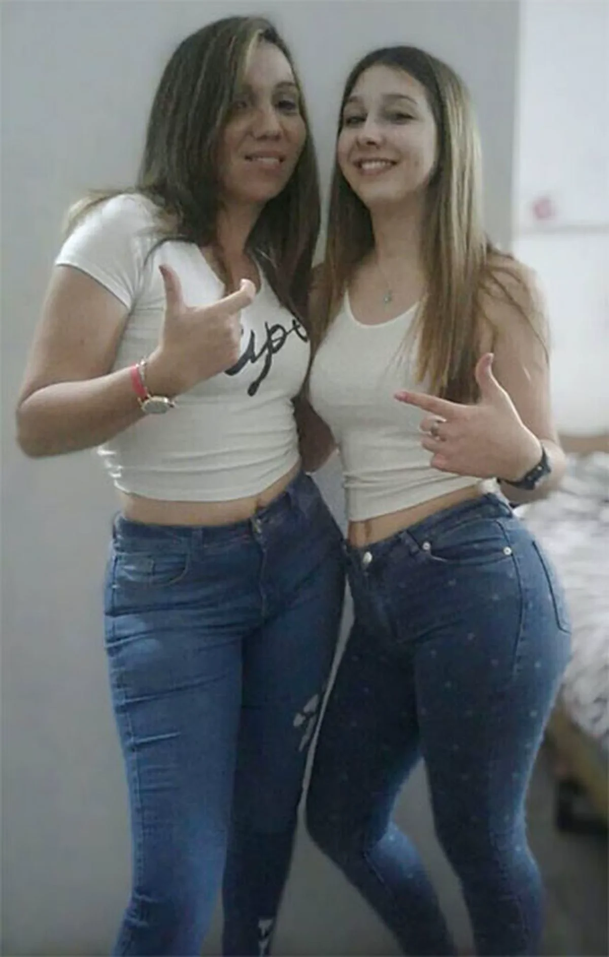 Dos chicas jóvenes con remera blanca y jeans posan sonriendo en una habitación.