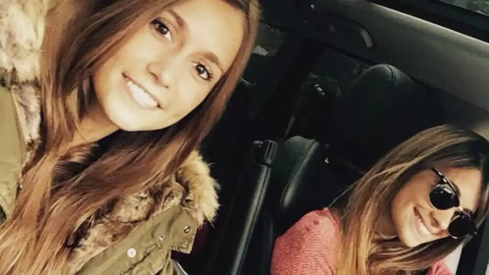 Dos mujeres sonriendo adentro de un auto, una con campera de abrigo y la otra con anteojos de sol.