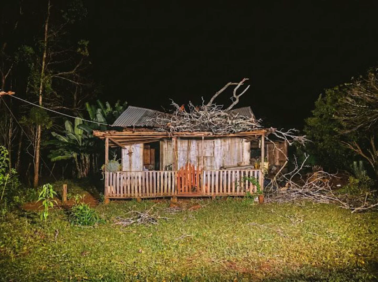 Casilla de madera con ramas caídas sobre el techo de chapa en un terreno descampado de noche.