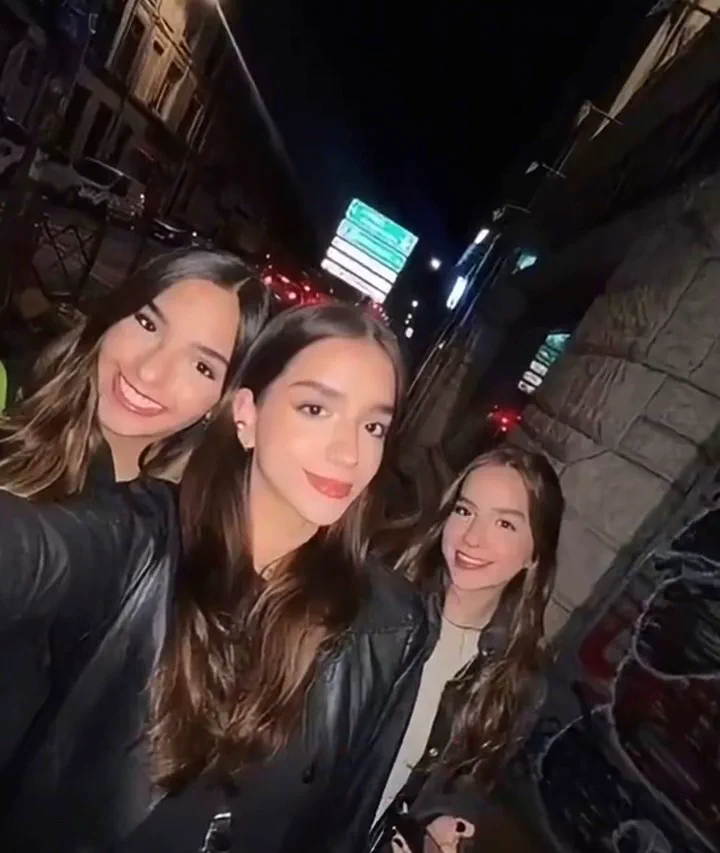 Tres chicas jóvenes posan sonrientes para una selfi nocturna en una calle de la ciudad.