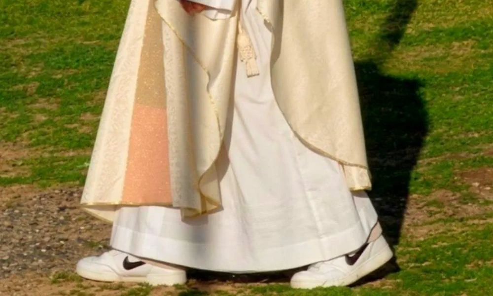La parte inferior de una túnica litúrgica blanca y dorada con zapatillas deportivas en un parque.