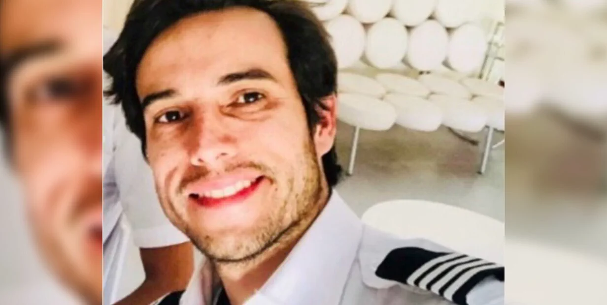 Un hombre con uniforme de piloto de camisa clara y charreteras sonriendo en un primer plano.
