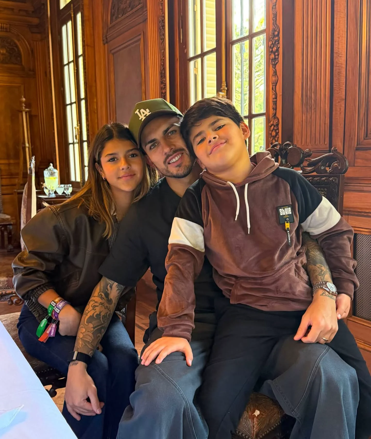 Leandro Paredes posa abrazado junto a sus dos hijos en un ambiente con paneles de madera.