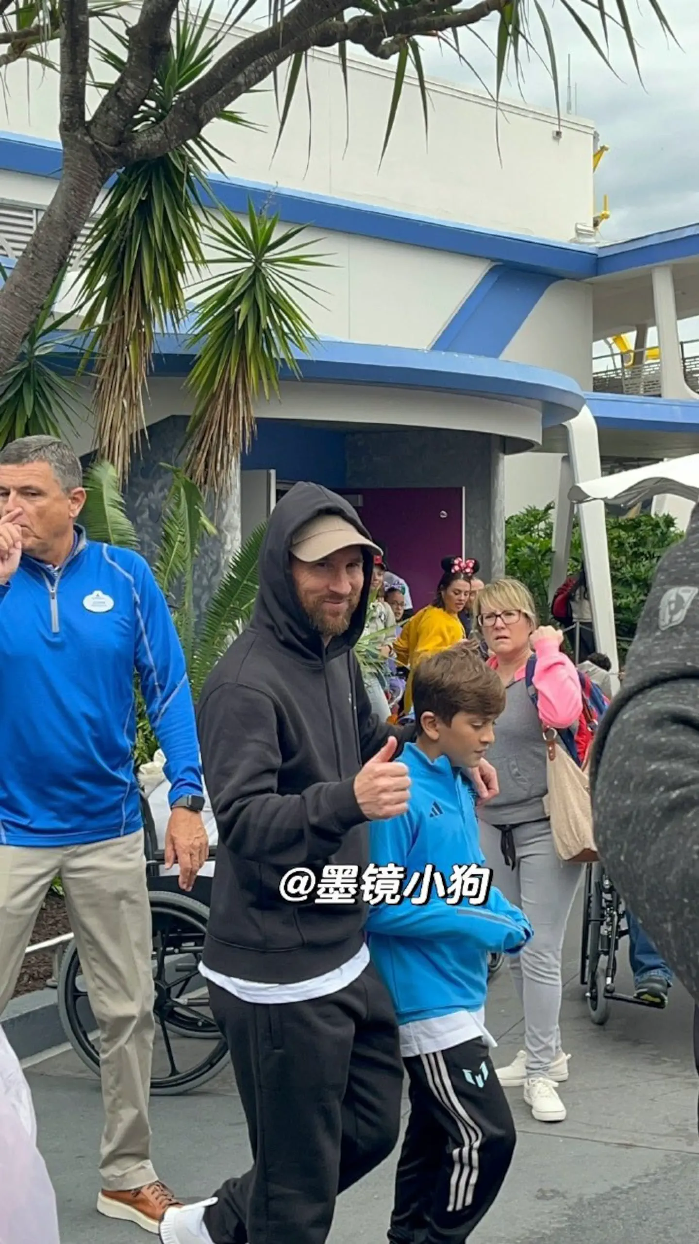 Lionel Messi sonríe y levanta el pulgar mientras camina junto a un nene cerca de un edificio.