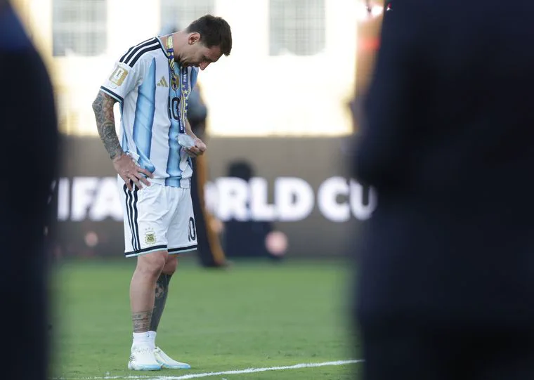 Lionel Messi con la cabeza baja y una medalla al cuello parado sobre el césped de una cancha.
