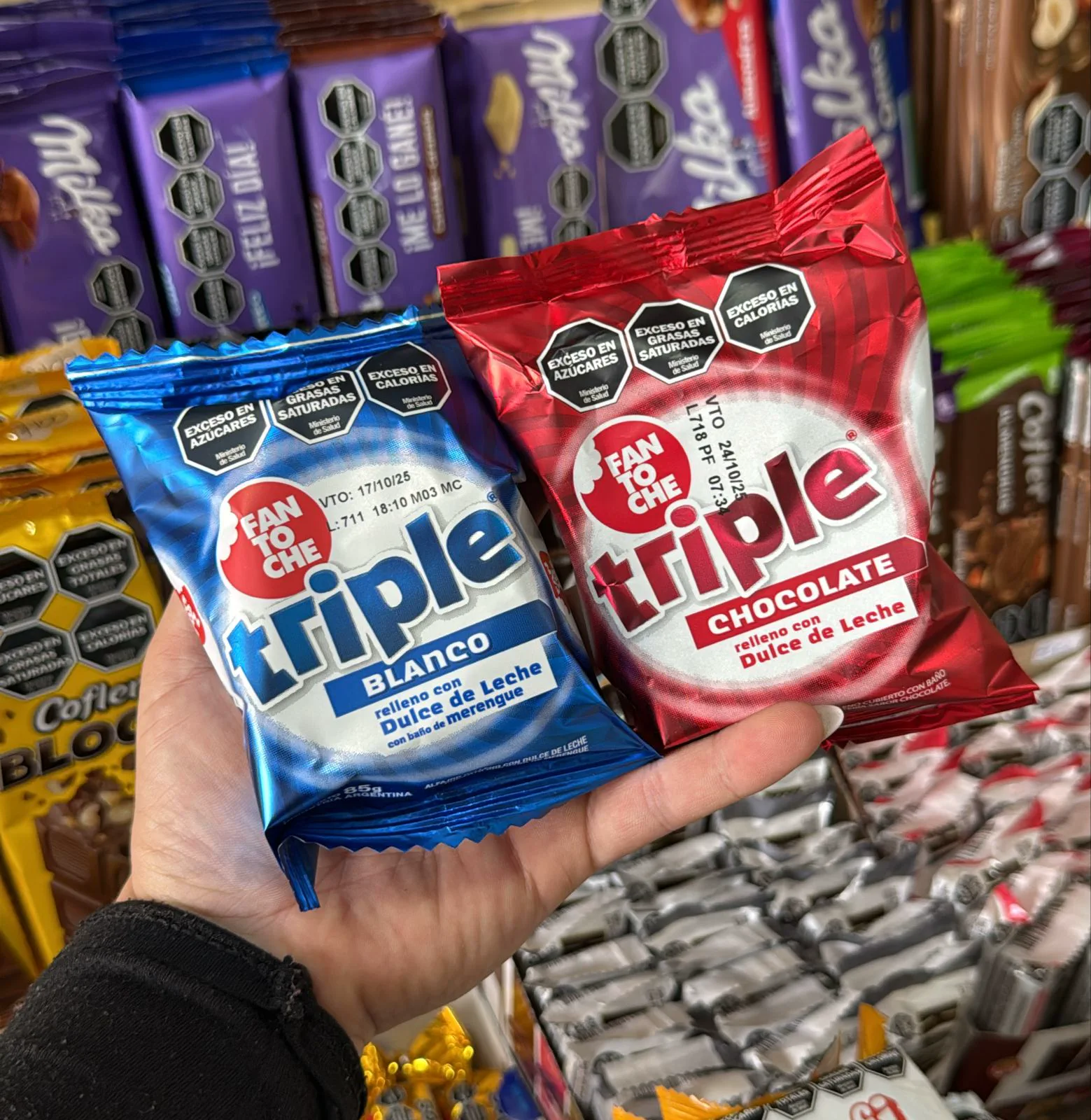 Una mano sostiene dos paquetes de alfajores triples Fantoche, uno blanco y otro de chocolate.