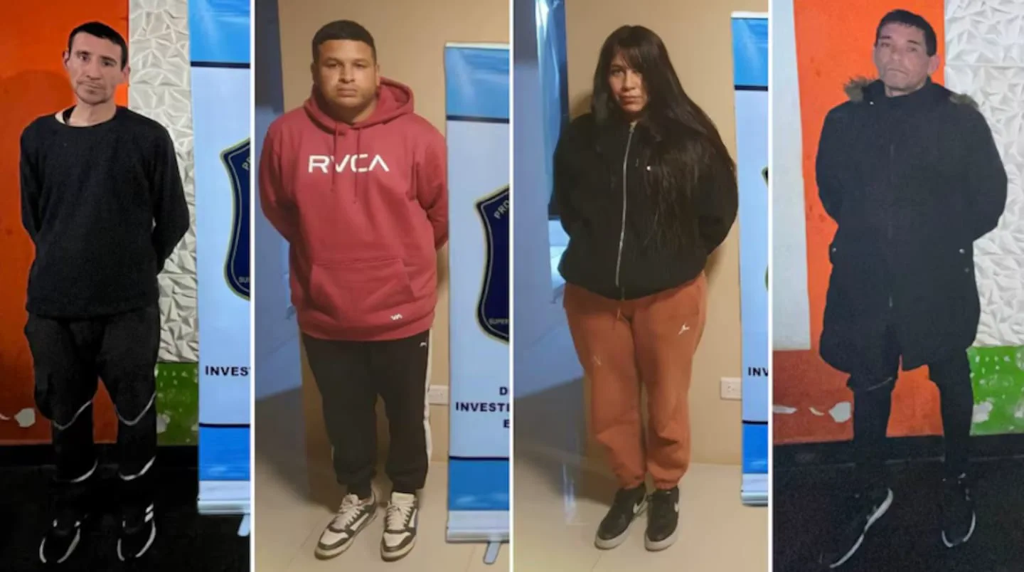 Tres hombres y una mujer posan parados frente a pancartas policiales durante una detención.