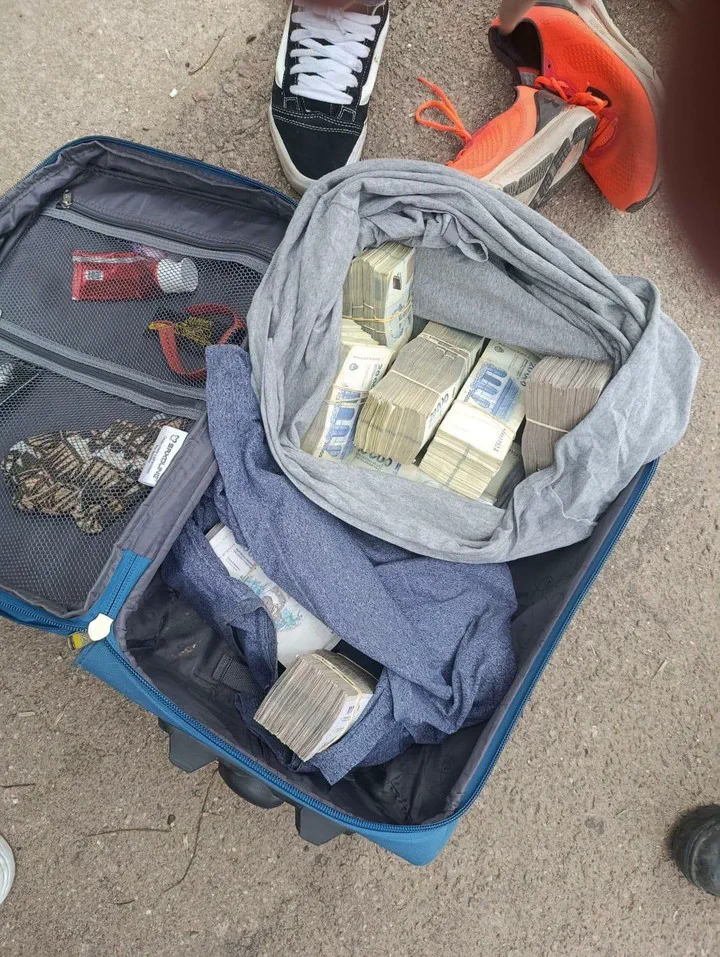 Valija abierta en el suelo con fajos de billetes entre prendas de vestir.