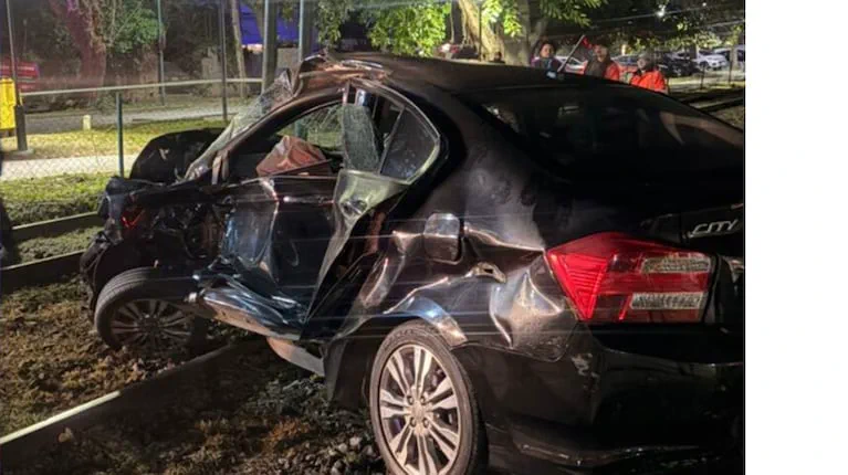 Un auto negro chocado con la puerta trasera y el techo abollados está sobre las vías del tren.