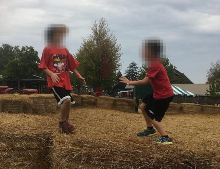 Dos nenes en remera roja y pantalones cortos juegan arriba de fardos de pasto seco al aire libre.