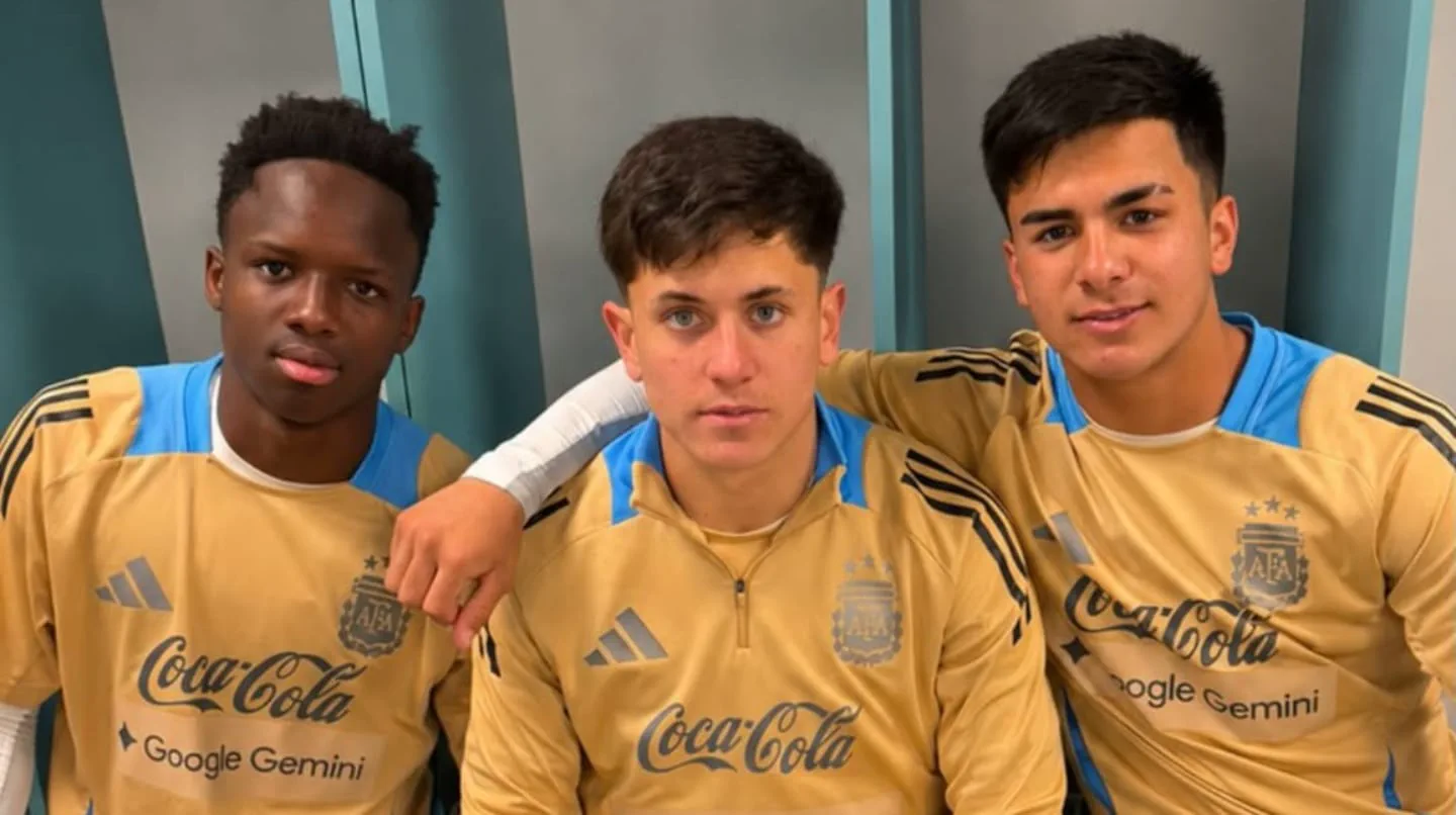 Tres jugadores jóvenes posan abrazados con indumentaria dorada de la selección argentina de fútbol.