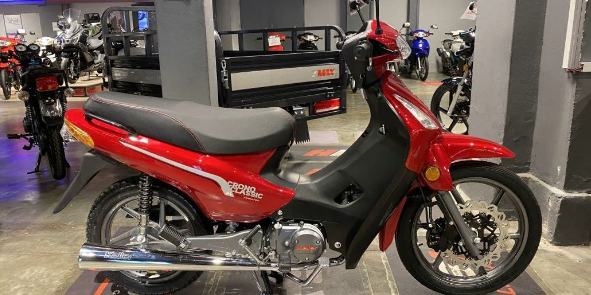Moto roja estacionada en un salon de ventas con otros vehiculos de fondo.