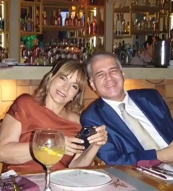 Un hombre de traje y una mujer sentados a una mesa de restaurante sonríen mirando al frente.