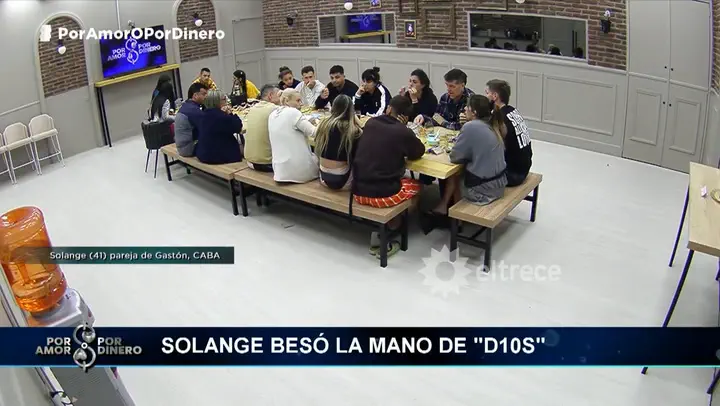 Un grupo de personas está sentado alrededor de una mesa larga comiendo en el set del programa Por amor o por dinero.