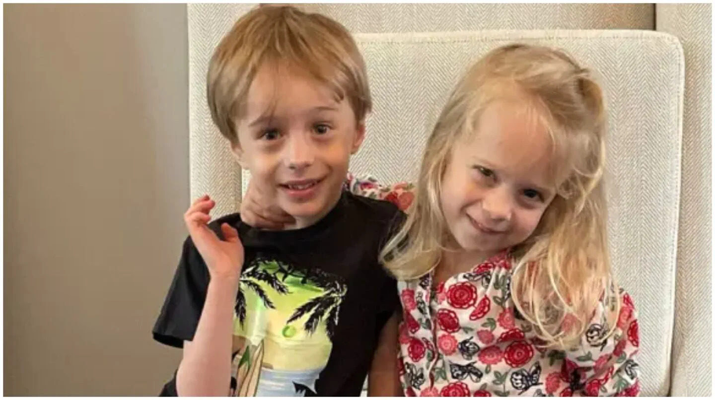 Dos nenes sonrien sentados juntos frente a la camara.