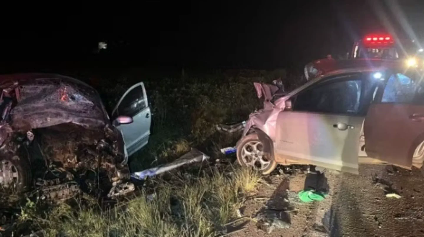 Dos autos destrozados tras un choque frontal nocturno con restos esparcidos sobre el pasto y el asfalto.