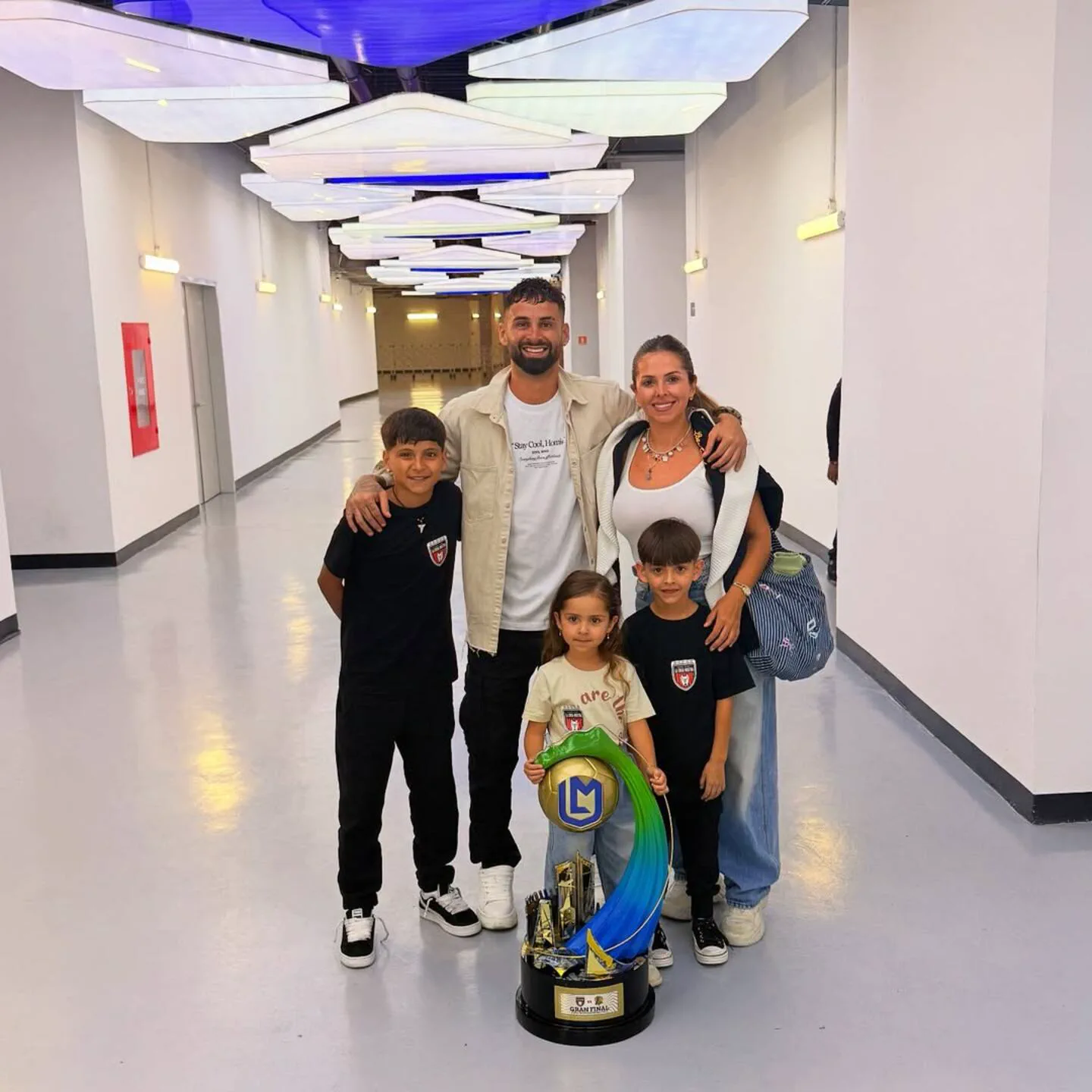 Un hombre, una mujer y tres chicos posan en un pasillo iluminado con un trofeo.