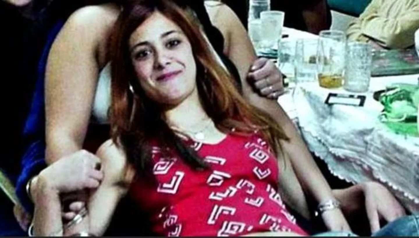 Una chica con remera roja estampada sonríe sentada junto a otra persona en una mesa con vasos.