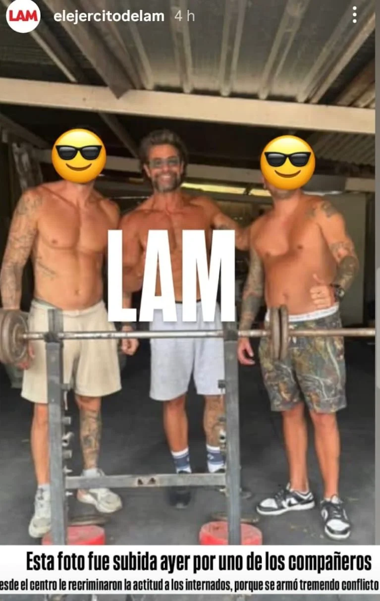 Tres hombres en bermudas posan detras de una barra de pesas en un gimnasio.