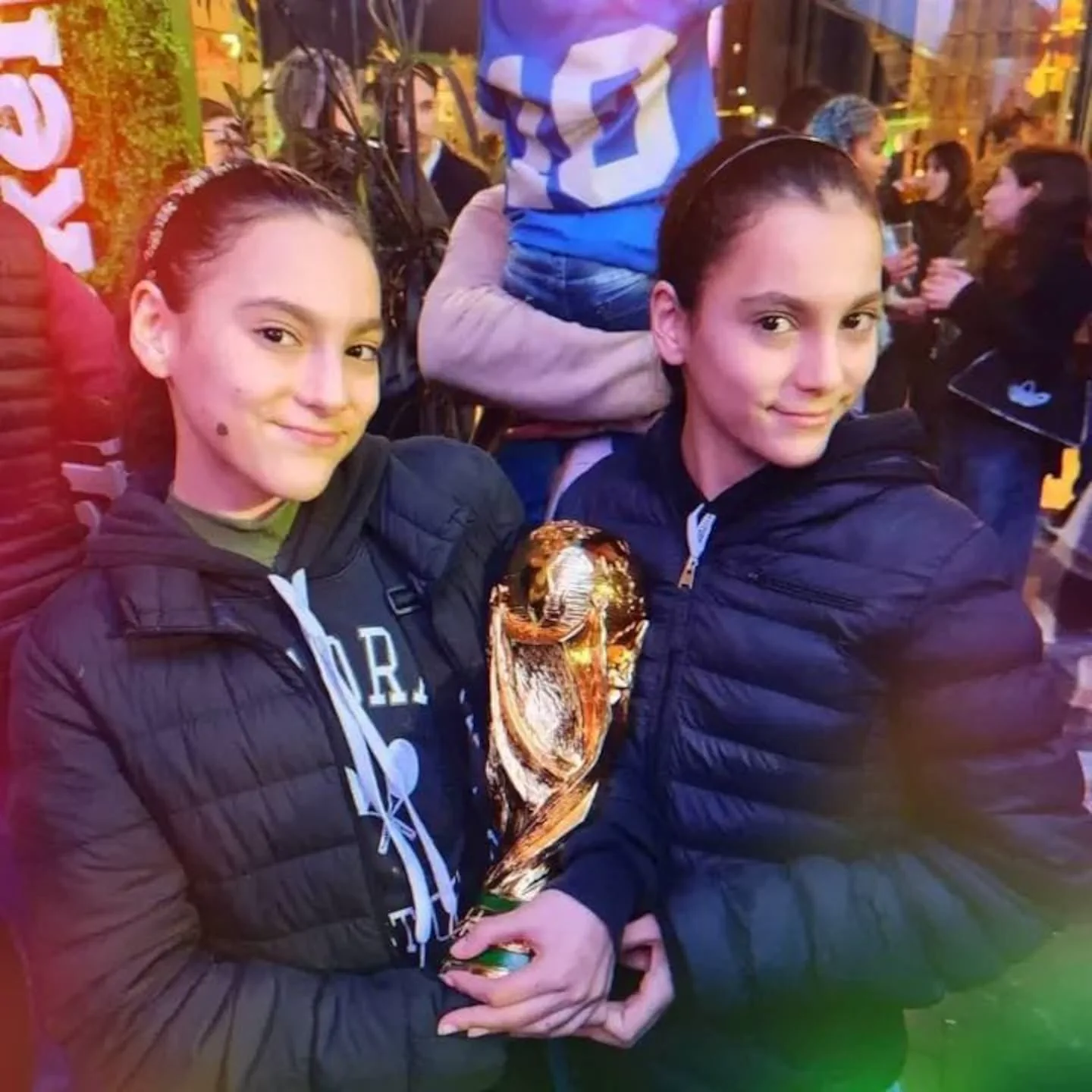 Dos chicas sostienen juntas una réplica dorada del trofeo de la Copa del Mundo en la calle.