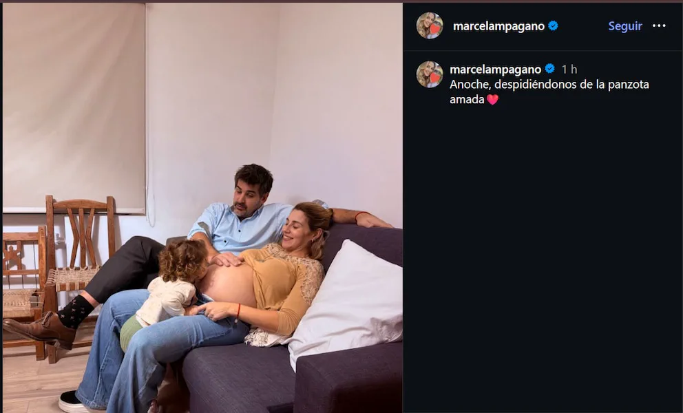 Marcela Pagano embarazada en un sillón junto a un hombre mientras una nena le da un beso en la panza.