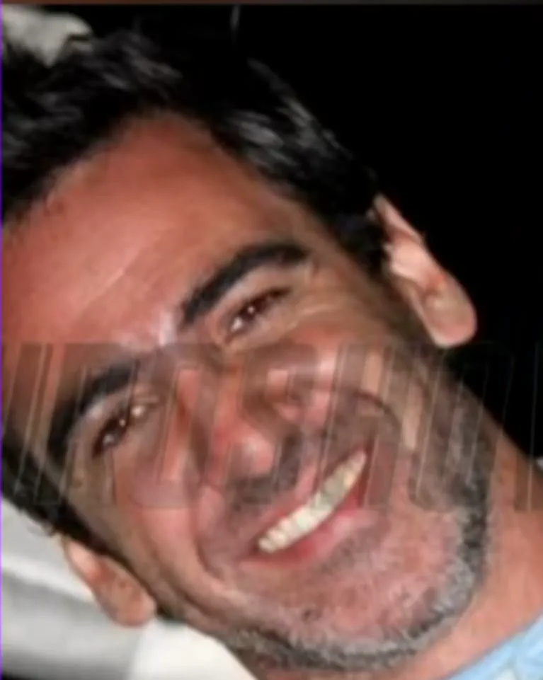 Primer plano de la cara inclinada de un hombre con barba corta y sonrisa abierta.