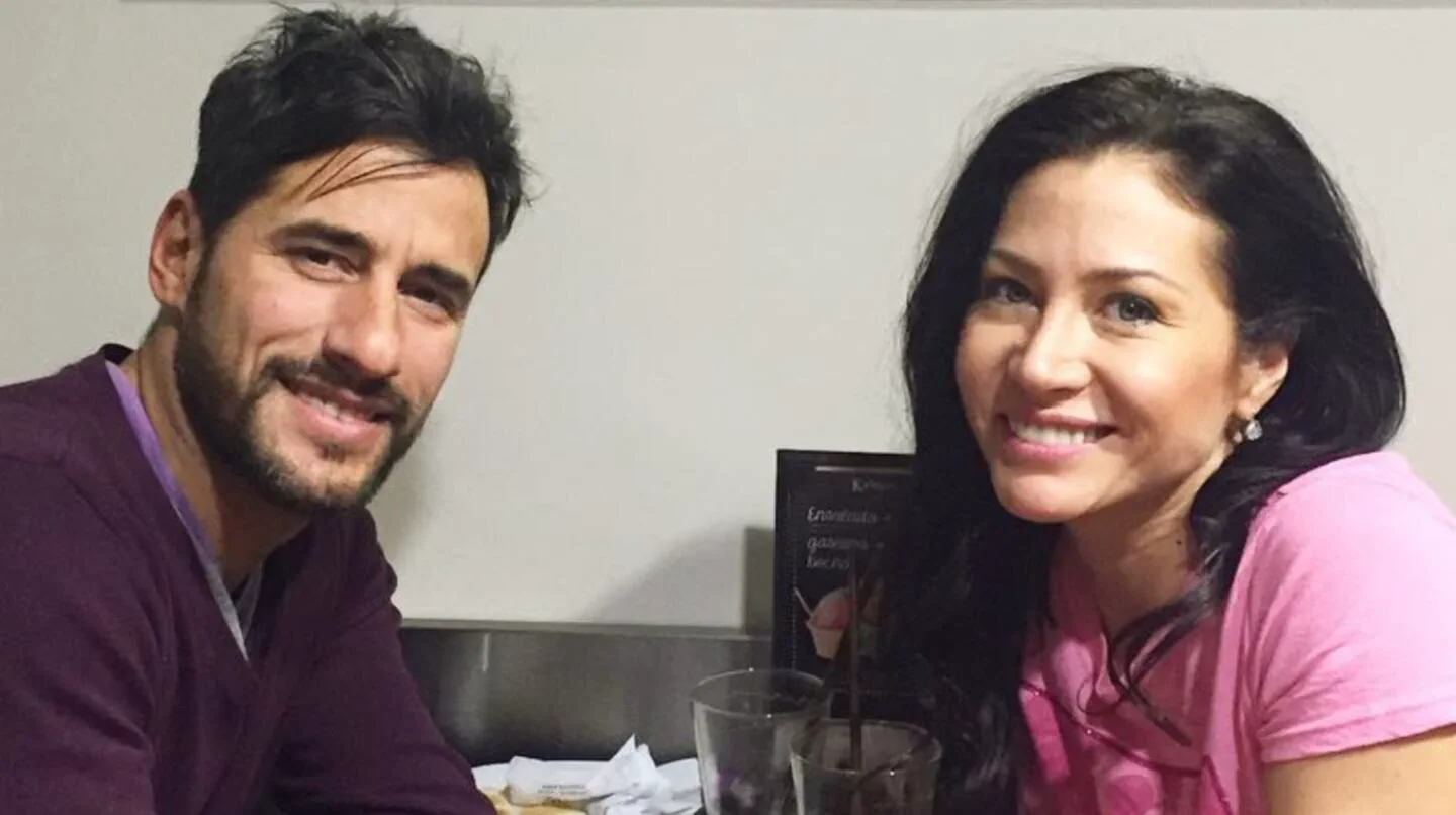 Un hombre y una mujer sentados juntos a la mesa de un bar o restaurante sonríen a la cámara.