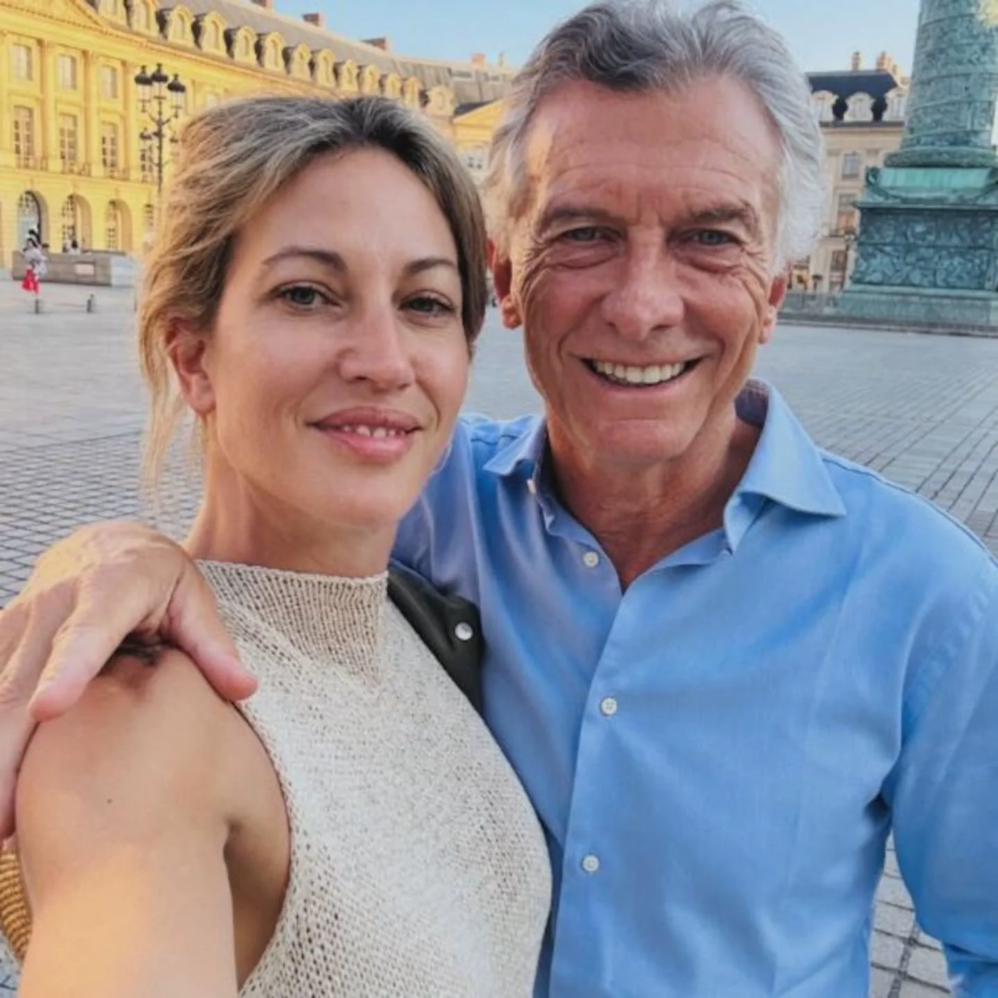 Mauricio Macri y Juliana Awada se sacan una selfi sonriendo al aire libre en una plaza adoquinada.