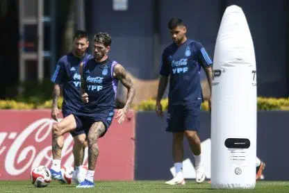 Rodrigo De Paul, Lionel Messi y Cristian Romero entrenando con ropa deportiva azul en una cancha de fútbol.