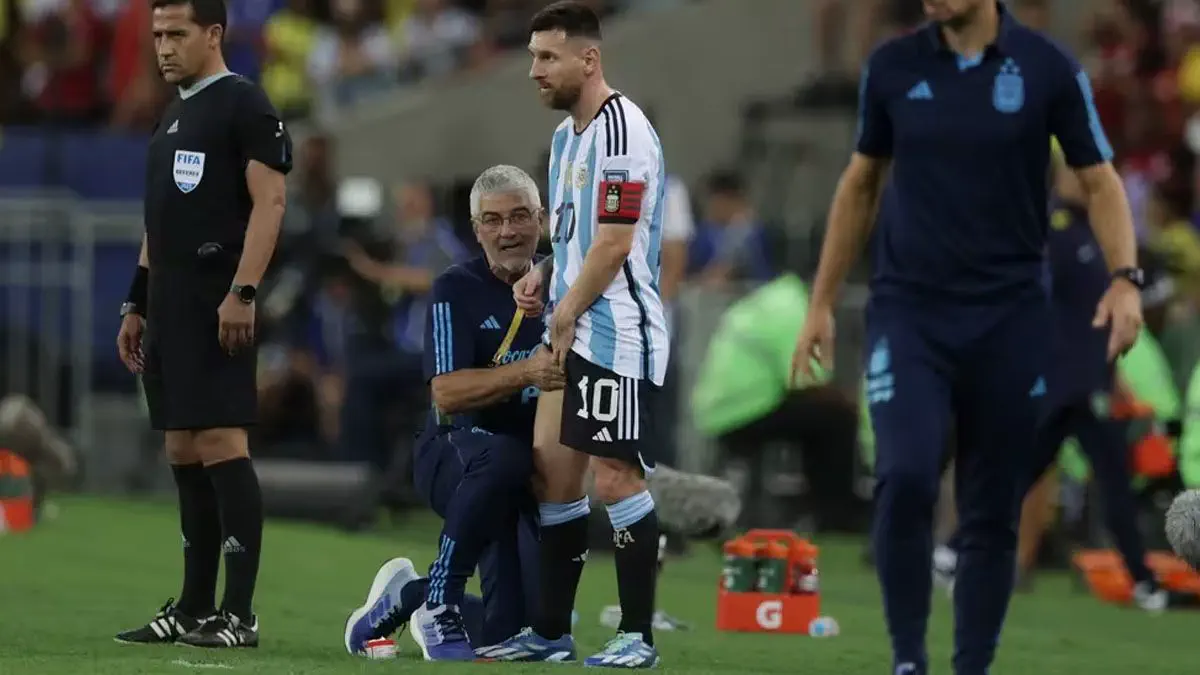 Lionel Messi recibe atención del fisioterapeuta de la selección argentina en una pierna durante un partido de fútbol.