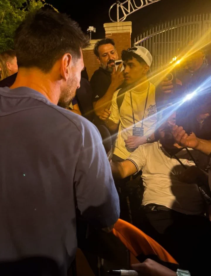 Lionel Messi de espaldas firmando autógrafos rodeado de personas durante la noche.