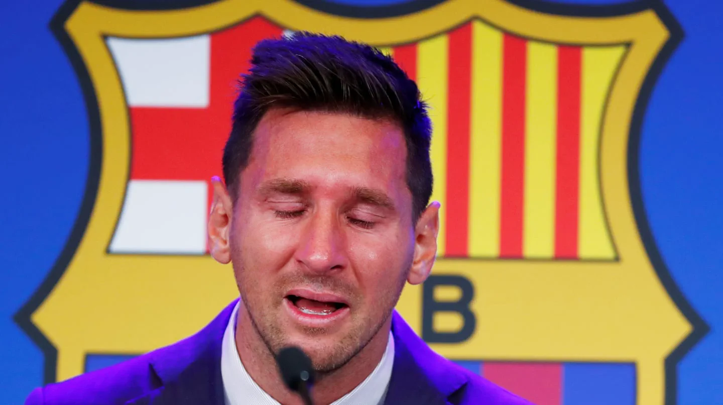 Lionel Messi llora con los ojos cerrados frente a un micrófono y el escudo de fondo del Barcelona.