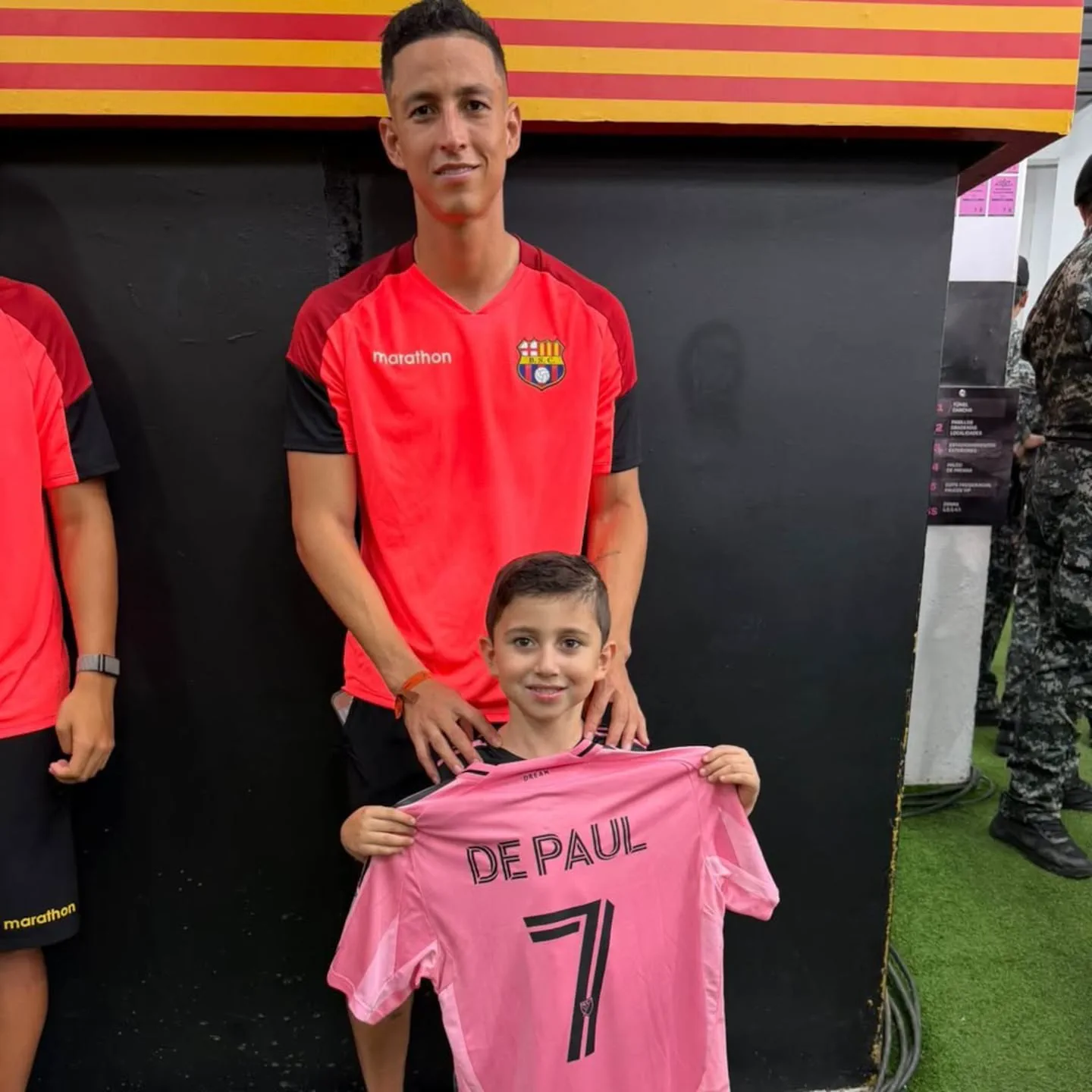 Un hombre con remera deportiva roja posa junto a un nene que sostiene una camiseta rosa con el número siete.
