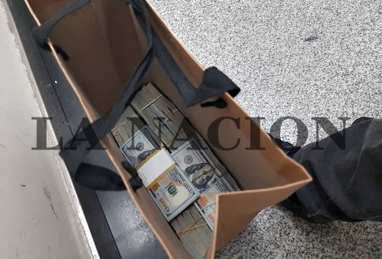 Varios fajos de billetes de cien dólares acomodados adentro de una bolsa de papel con manijas.