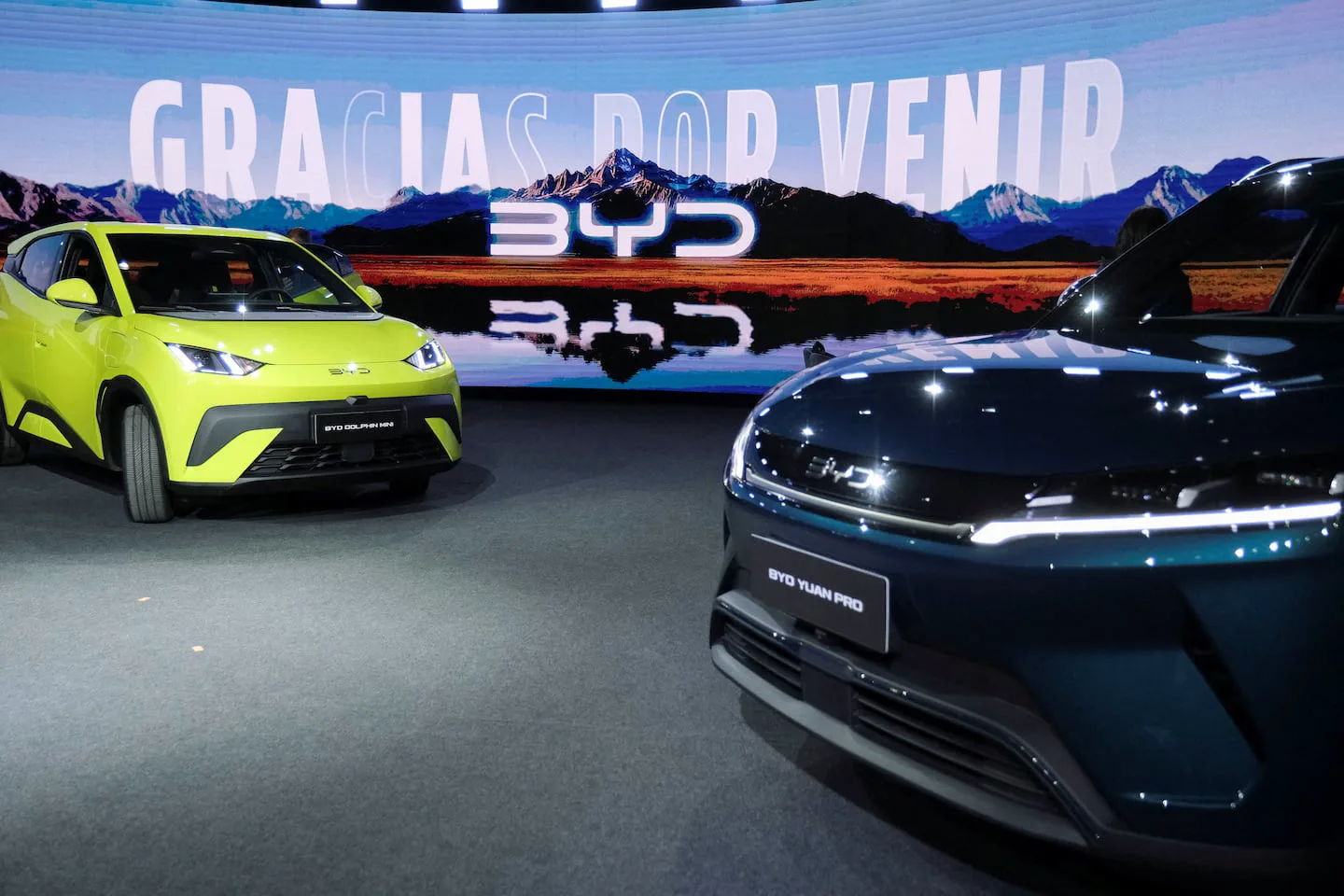 Dos autos eléctricos sobre una tarima frente a una pantalla con un paisaje y la marca BYD.