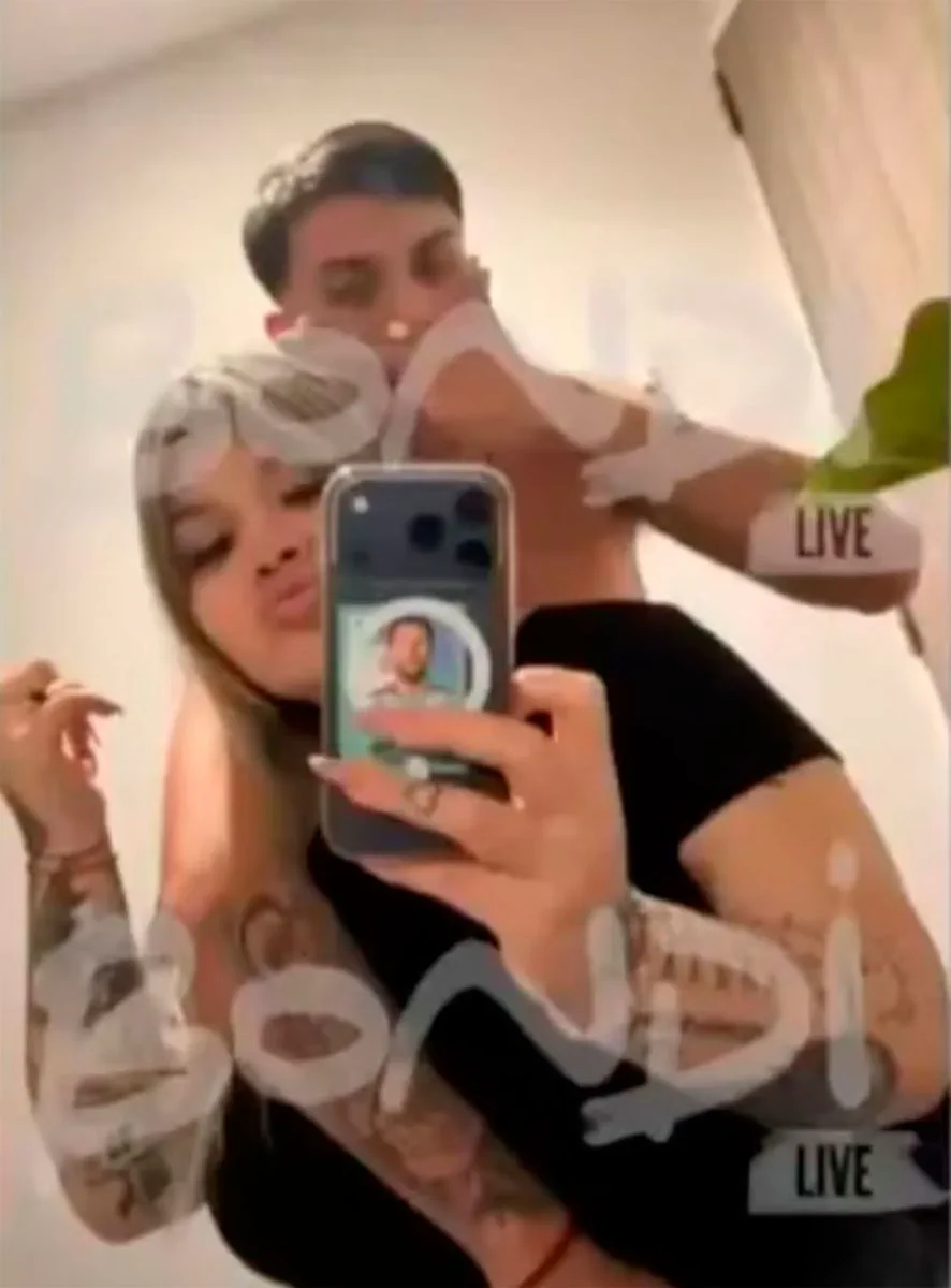 Una chica se saca una selfie frente a un espejo mientras un joven la abraza por la espalda.