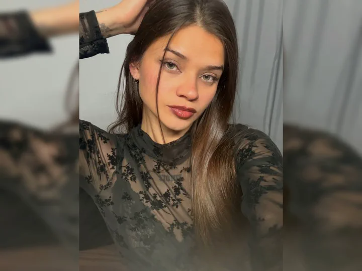 Una joven de pelo castaño posa mirando a cámara con una remera negra de encaje transparente.